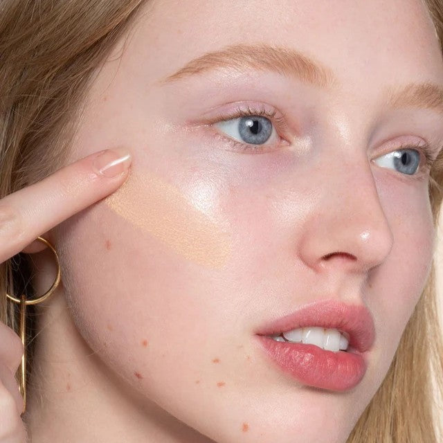 A woman applies a serum foundation on her face
