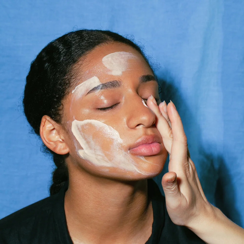 Cleansing Balm von Mádara - aufgetragen auf Gesicht, vor blauem Hintergrund