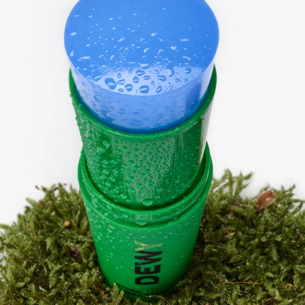 Dewy Hydra Caffeine Serum Stick von Mádara - geöffnet, steht auf feuchtem Moos