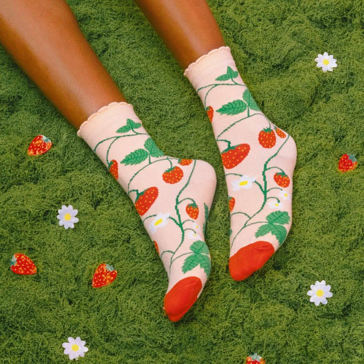 Strawberry Plant Socks von Coucou Suzette - getragen, grüner Hintergrund mit Blümchen- und Erdbeerspangen