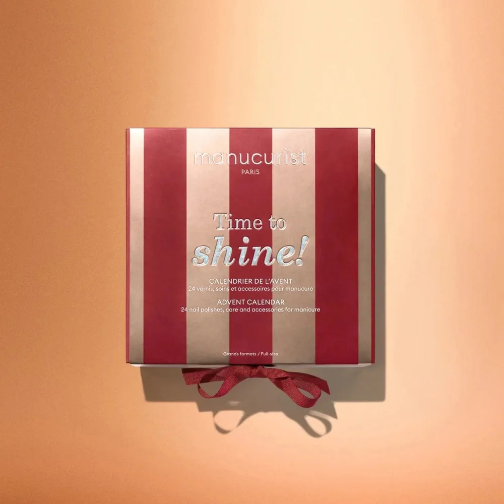 Manucurist Adventskalender 2026 Time to Shine in rot-goldener Verpackung vor orangefarbenem Hintergrund