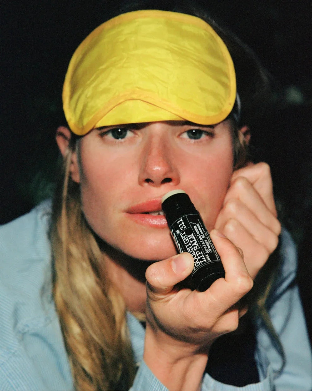 Frau mit gelber Schlafmaske trägt den L:A Bruket Goodnight Lip Balm auf die Lippen auf