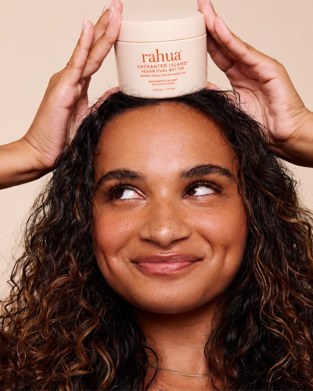 Frau mit natürlichem Lockenhaar verwendet Rahua Enchanted Island Vegan Curl Butter