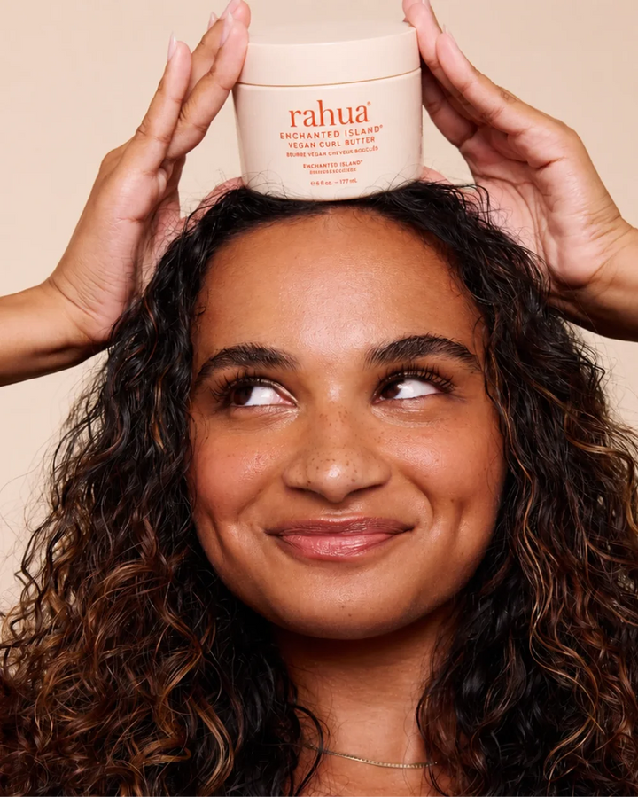 Frau mit natürlichem Lockenhaar verwendet Rahua Enchanted Island Vegan Curl Butter