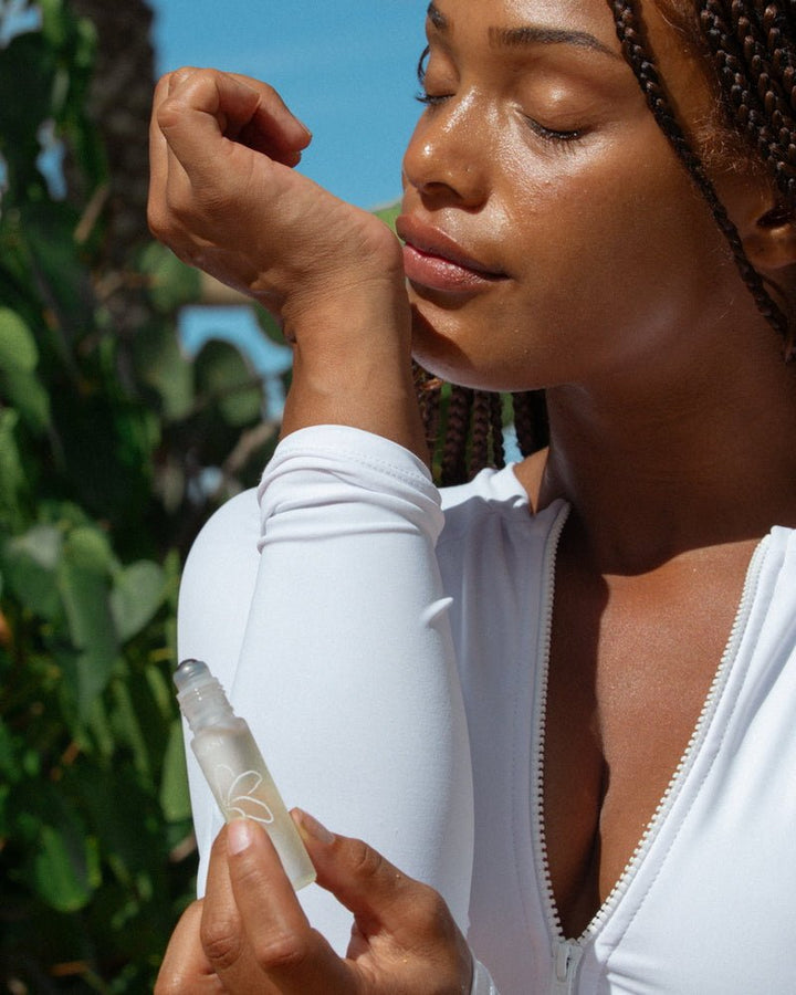 Leahlani Pua Lei Perfume Oil – Detailaufnahme: Person riecht am Handgelenk, Flakon im Vordergrund
