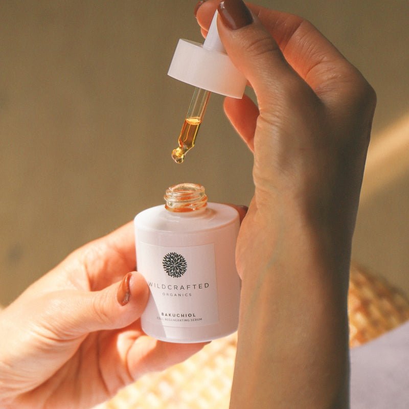 Hände halten Wildcrafted Organics Bakuchiol Cell-Regenerating Serum Flasche mit Pipette, die goldene Serumtropfen abgibt