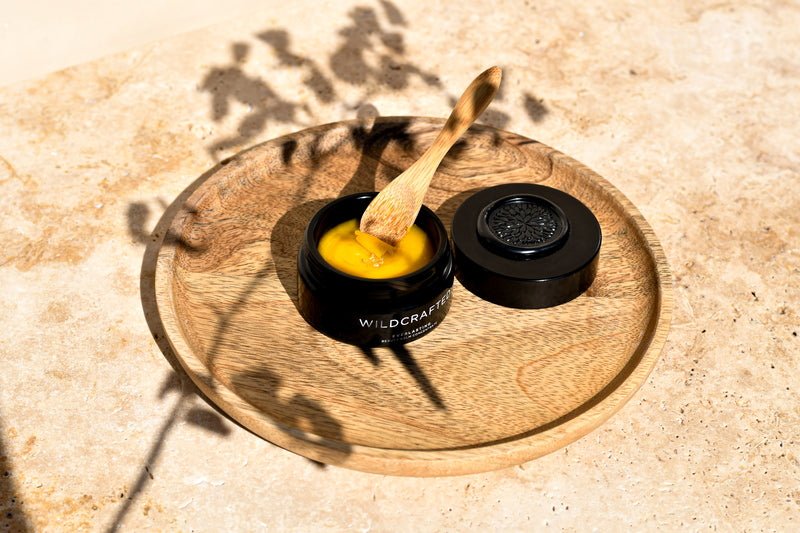Wildcrafted Organics Everlasting Beauty Balm Tiegel mit Holzspatel auf runder Holzschale - Stimmungsbild