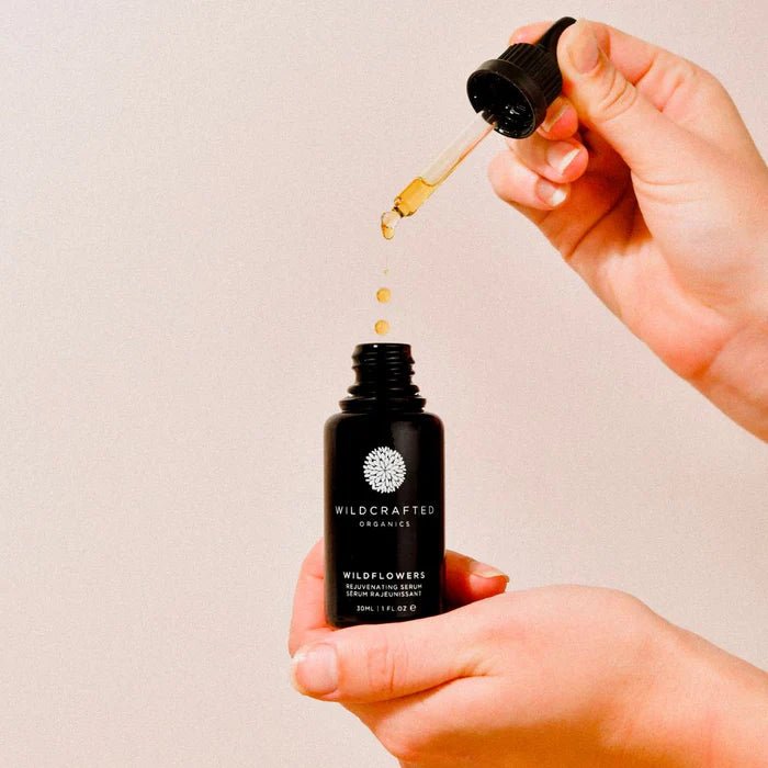 Hände halten Wildcrafted Organics Wildflowers Rejuvenating Serum Flasche mit Pipette, die goldene Serumtropfen abgibt